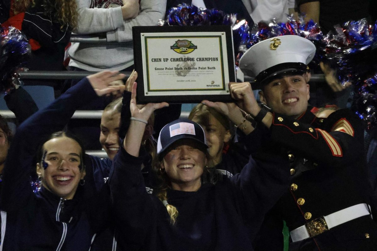  Milly Bellamy ’24, Katie VandeWyngearde ’24 and a marine gather around the certificate showing that South beat North in the chin-up competition. The student section erupts in cheer when it was announced.