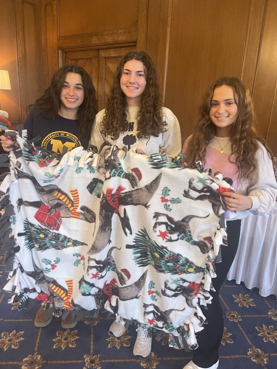 Students Eleni Melhelm24, Alex Lupo26, and Ella Telegadas 24 holding up their finished blanket during a blanket making meeting at the Country Club of Detroit.