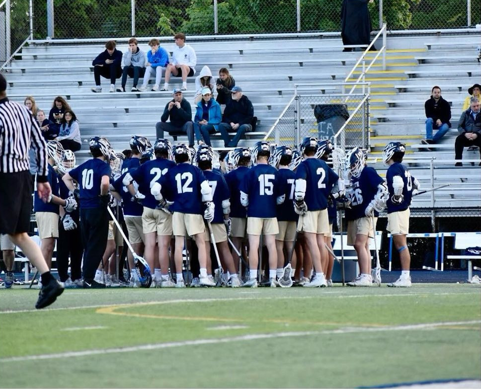 Grosse pointe south boys varsity lacrosse team stands on the sideline during a time out, ready to attack.