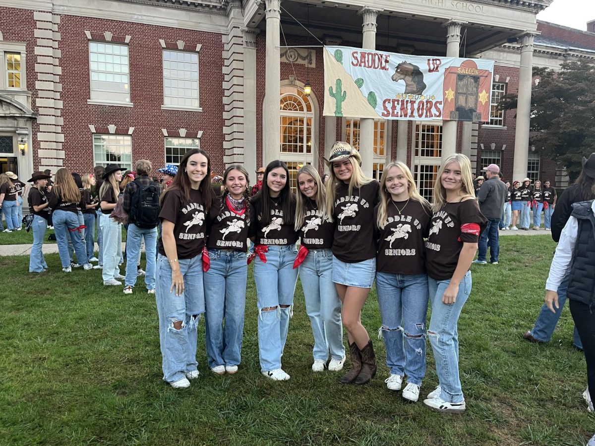 Sarah Cook, Ruby Berger, Trulyn Doyle, Lucy Stidham, Evie Smith, Olivia McMillin, and Scout Webber, all ’25, smile for a picture under their senior banner. 