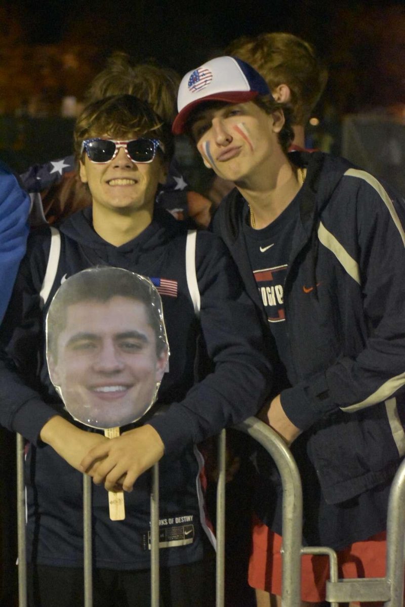 Johnny Klepp ’25 and Luca Parlangeli ’25 hold a fat head of Josh Lemanski ’25 as they cheer the players on. (Photo courtesy of Thomas Brieden '25)
