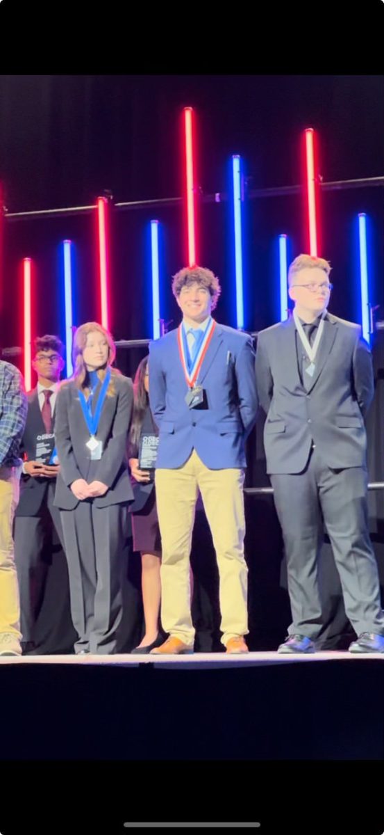 DECA President CJ Rehani ’25 (center) stands on stage at states in 2024. Rehani won the state title for Principles of Business Management (photo courtesy of CJ Rehani '25).