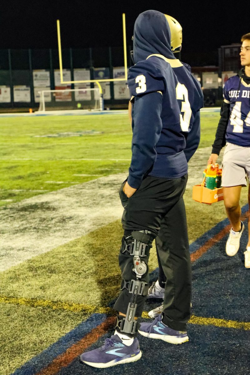 Sidelined: Charlie Bedsworth ’27 stands on the sideline during the Homecoming game against Lakeview. He watches the game after suffering a season-ending injury to his leg.