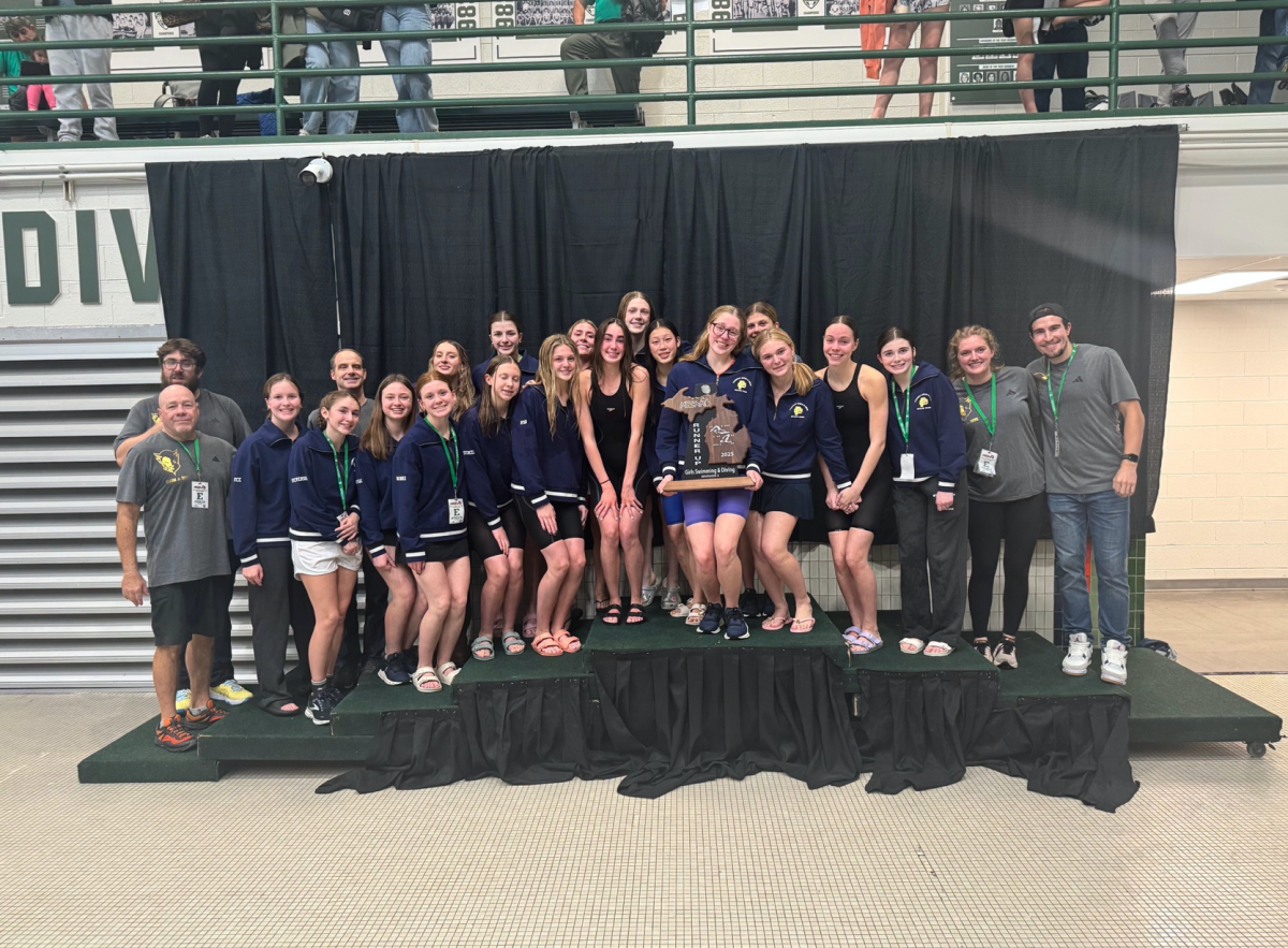 The girls swim team, accompanied by their coaches, stands on the podium holding their runner-up trophy. They finished in second place 2 points short of winning the meet.